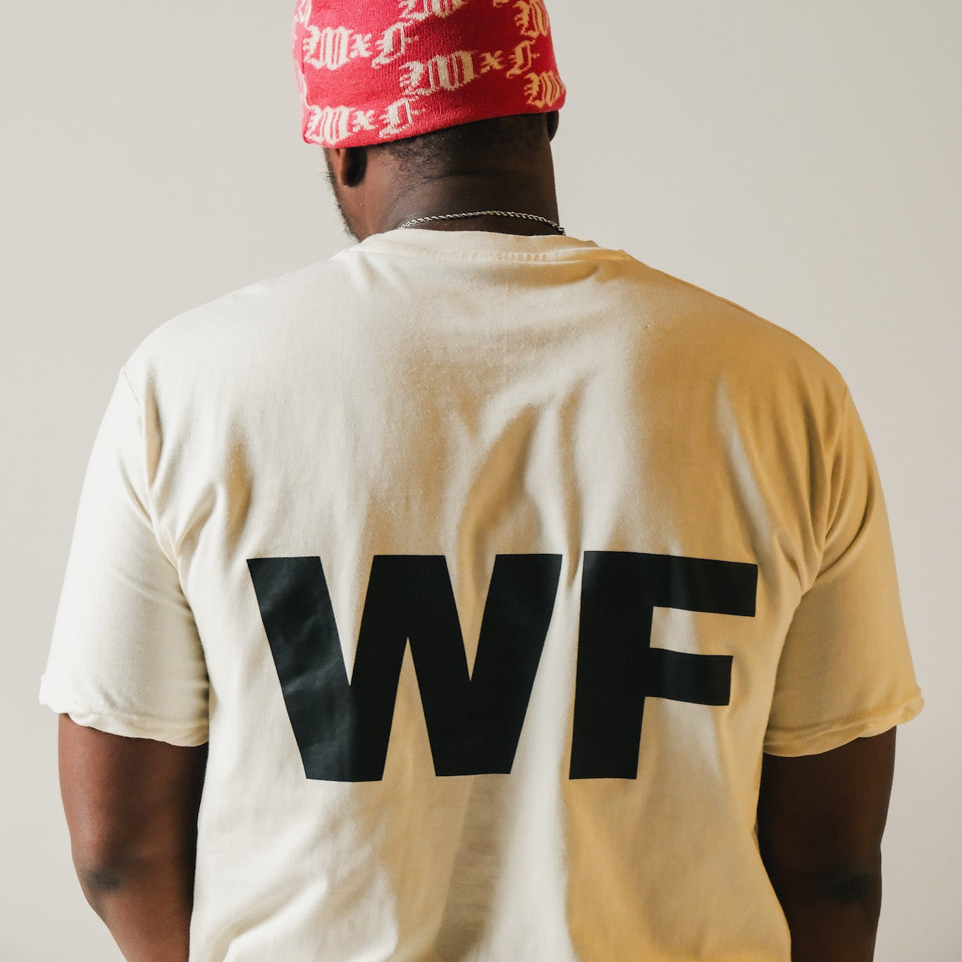 Model wearing a red beanie and white t-shirt with 'WF' on the back against a plain background