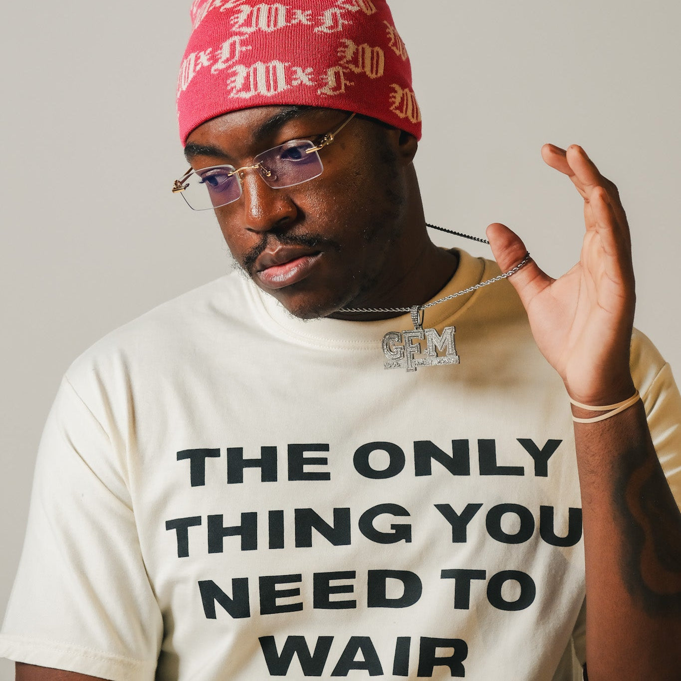 Model wearing a pink beanie and a white t-shirt with text, The Only Thing You Need To Wair, against a plain background